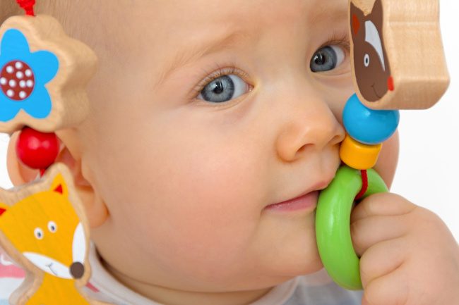 Baby spielt mit buntem Holzspielzeug. Was süß und knuffig aussieht, ist wichtiger Teil der Entwicklung des Kindes.